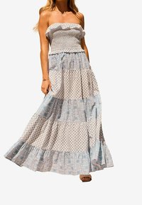 Maxiklänning med veckad bodice, lager av volanger och ett blommönster i blått och vitt. Lättviktig tyg, utan axelband.