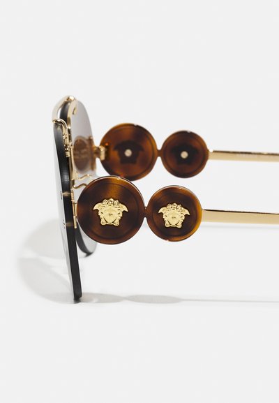 Brown and black sunglasses with gold hardware. The frame features circular, tortoiseshell accents with embossed head details on the temples.