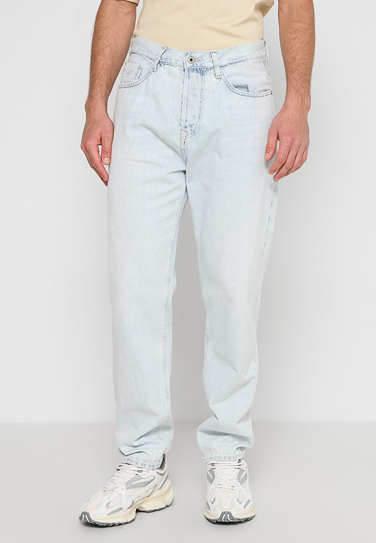 Hellblaue Denim-Jeans mit lockerer Passform, Fünf-Taschen-Design und zarter Ausbleichung, kombiniert mit beigen Sneakers und einem passenden Oberteil.