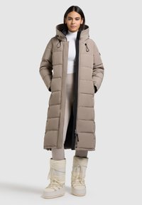 Gevoerde lange jas in lichtbruin met een capuchon, voorzien van een rits aan de voorkant en trekkoordaccenten. Gekleed met witte, veterschoenen voor de winter.