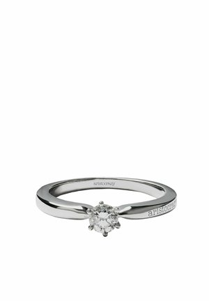 Anillo de plata con un diamante central redondo y facetado, con una banda lisa y un sutil grabado de la marca en un lado.