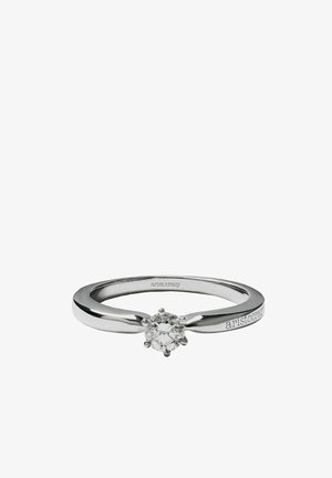 Anillo de plata con un diamante central redondo y facetado, con una banda lisa y un sutil grabado de la marca en un lado.