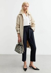 Beige trenchcoat, witte blouse, donkere broek met strik taille, zwarte puntige ballerina's en een kleine zwart-witte handtas met slangenprint.