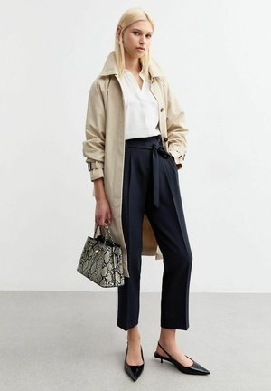 Beige trenchcoat, witte blouse, donkere broek met strik taille, zwarte puntige ballerina's en een kleine zwart-witte handtas met slangenprint.