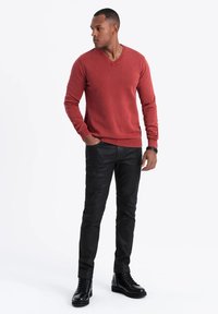 Czerwony sweter w serek, dopasowany, z długimi rękawami i ściągaczami; połączony z czarnymi, dopasowanymi skórzanymi spodniami oraz czarnymi wiązanymi botkami.