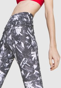 Leggings noirs taille haute avec un imprimé graphique de formes abstraites blanches et de texte, présentant une texture lisse et une taille élastique.