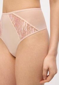 Μπεζ εσώρουχο με ψηλή μέση και ροζ διακοσμητικά πάνελ από δίχτυ, φοράει ένα άτομο, με εμφανή το γοφό και το χέρι που ακουμπά δίπλα στον μηρό.