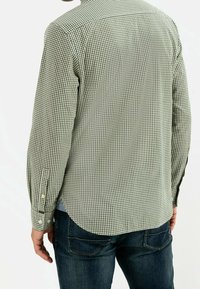 Camisa de manga larga a cuadros verdes y blancos con dobladillo curvado, puños abotonados y una textura suave, colocada sobre una persona que lleva vaqueros.