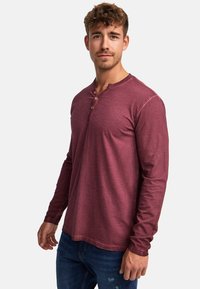 Burgunderfarbendes Langarm-Henley-Shirt mit drei Holzknöpfen, aus weichem, strukturiertem Stoff und mit lockerer Passform.