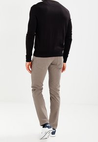 Zwarte trui met lange mouwen en geribbelde manchetten en zoom, gecombineerd met lichtgrijze slim-fit broek en witte sneakers met marineblauwe accenten.