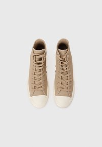 Beige színű, textúrált felületű anyagból készült magas szárú tornacipők, lapos fűzőkkel és fehér gumi orral.