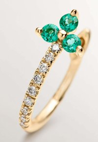 Anillo de oro con dos piedras preciosas verdes en la parte superior y una fila de diamantes más pequeños a lo largo de la banda, que presenta un diseño texturizado.
