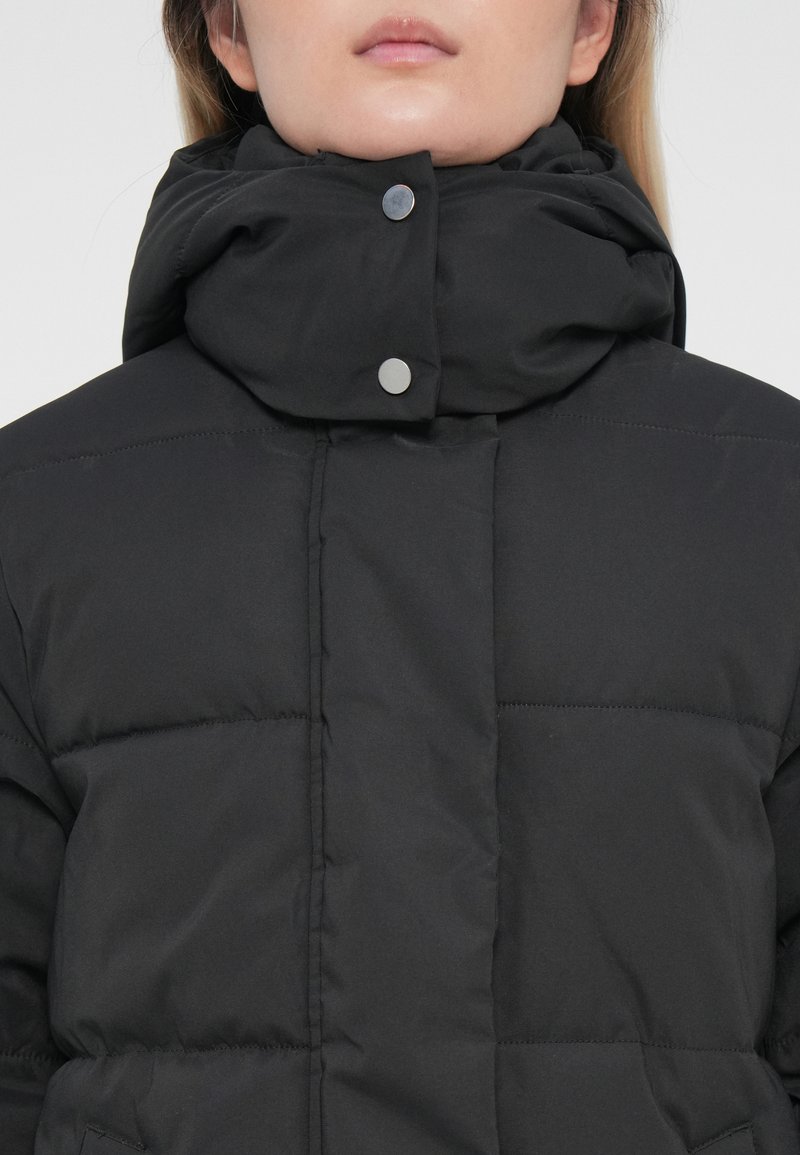 Schwarze Steppjacke mit hohem Kragen, silbernen Druckknöpfen und gestepptem Design. Der Stoff wirkt glatt und isoliert.