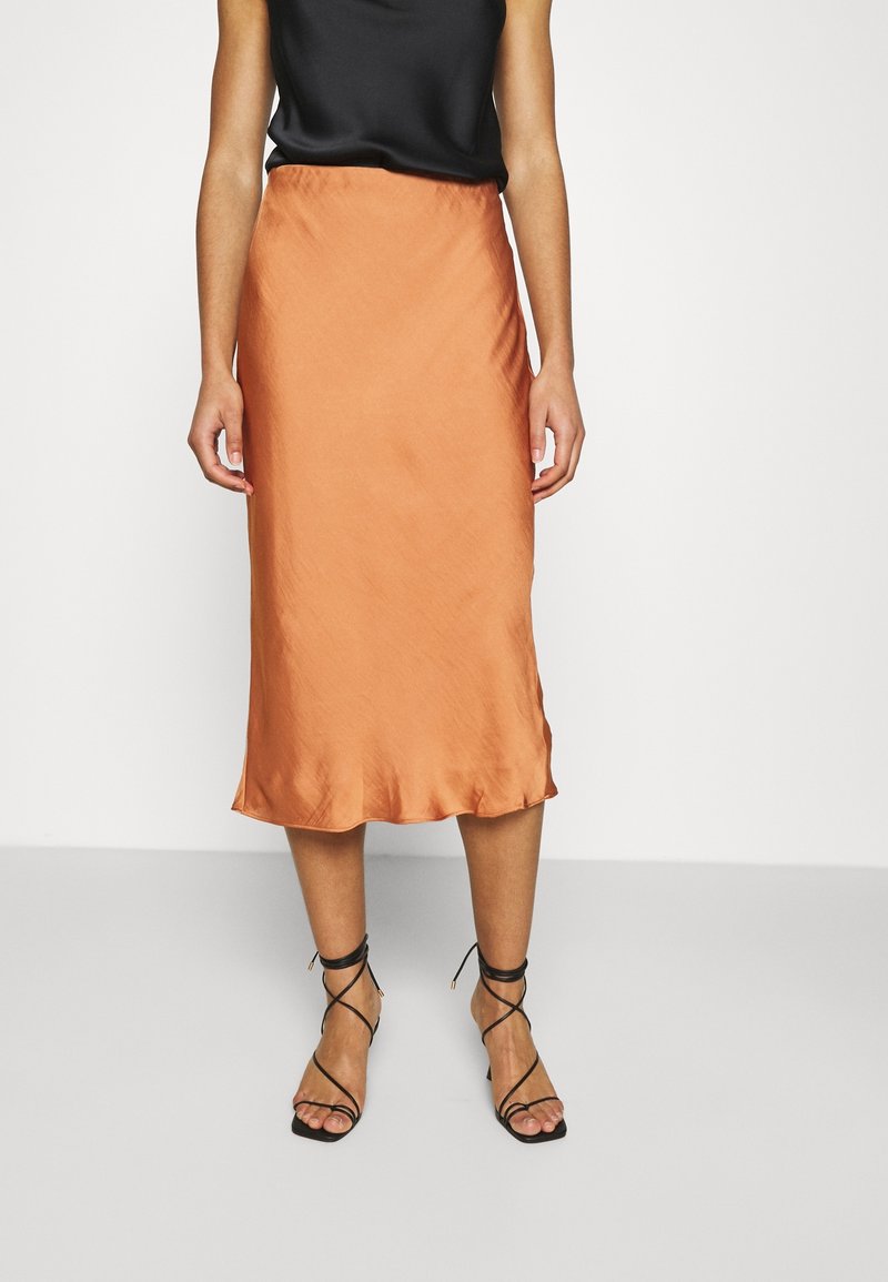 Saténová midi sukně v barvě spáleného oranžového, s hladkou texturou a vlnitým lemem. V kombinaci s černými sandály na řemínky.