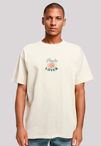 Crème-kleurig katoen t-shirt met korte mouwen, voorzien van een geborduurd ontwerp van pasta en de tekst "Pasta Liefhebber" in groen en oranje.
