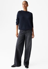 Maglione a coste blu navy con scollatura rotonda, abbinato a jeans grigi scuri a gamba larga. Scarpe nere con punta a stiletto completano l'outfit.