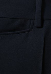 Primo piano di tessuto nero che mostra una tasca anteriore e un passante per cintura con cuciture visibili e dettagli della trama.