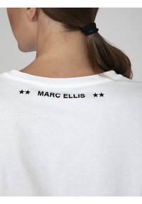Witte katoenen t-shirt met zwarte bedrukte tekst "MARC ELLIS" en twee sterren op de achterkant, met een ronde hals en korte mouwen.