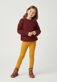 Bordowy sweter w sploty z grubego dziania, żółte legginsy i brązowe botki na sznurowadła. Sweter ma teksturowane wzory i luźny krój.