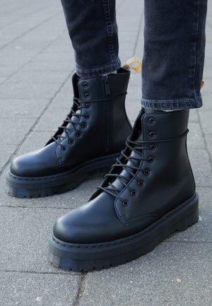 Czarne skórzane buty za kostkę z okrągłym noskiem, sznurowanym przodem i teksturowaną gumową podeszwą. Boczny zamek błyskawiczny i kontrastująca żółta pętelka ułatwiająca zakładanie.
