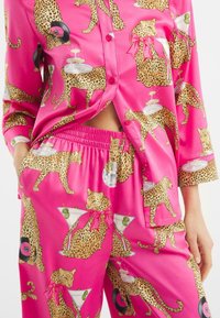 Růžový saténový pyžamový set s leopardím potiskem a hravými detaily, jako jsou sklenice na martini a gramofony. Obsahuje košili na knoflíky a elastický pas.