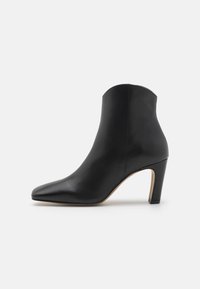 Bottine en cuir noir avec un bout pointu, une silhouette effilée et un talon de hauteur moyenne. Texture lisse, design minimaliste, tige sans détails.