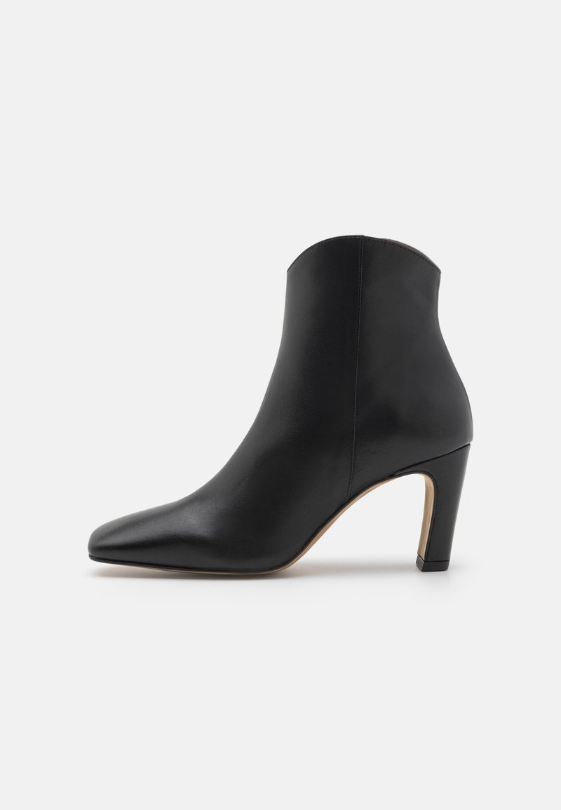 Bottine en cuir noir avec un bout pointu, une silhouette effilée et un talon de hauteur moyenne. Texture lisse, design minimaliste, tige sans détails.