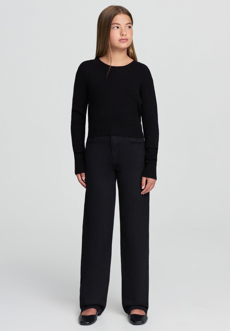 Czarny sweter dziany z okrągłym dekoltem, sparowany z czarnymi spodniami o szerokich nogawkach. Ubranie ma długie rękawy i luźny krój.