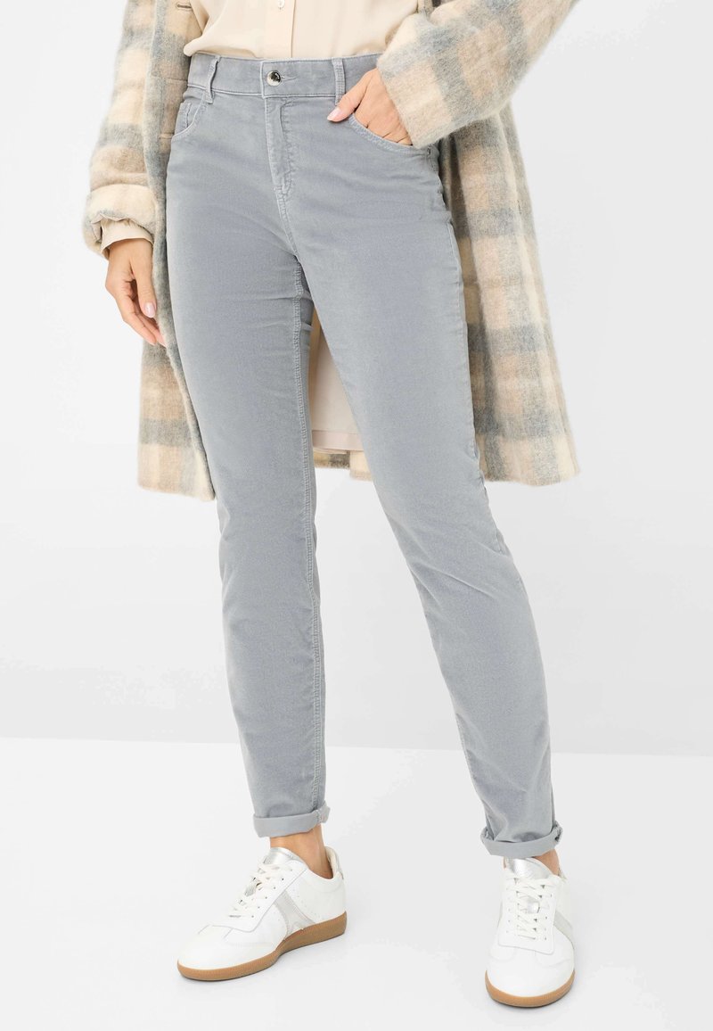 Pantaloni in corduroy grigi con vestibilità slim, dotati di tasche, chiusura con bottone e orli arrotolati, abbinati a scarpe sportive bianche.