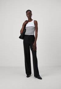 Débardeur blanc à rayures horizontales noires, associé à un pantalon large noir et des chaussures noires à enfiler, accessoirisé avec un sac noir.