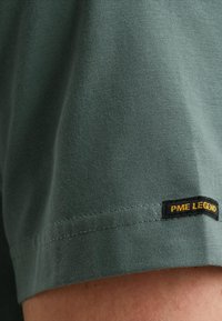 Groen katoenen T-shirt met een zachte textuur en korte mouwen, met een zwart label waarop "PME Legend" in geel staat op de zoom.