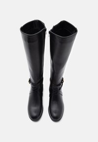 Polvisteitä yltävät mustat nahkasaappaat, joissa on sileä pinta, vinot nauhat korostavat ja sivuvetoketjut helpottavat pukeutumista.