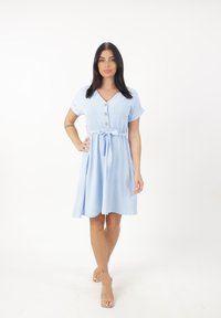 Abito azzurro chiaro lunghezza ginocchio con maniche corte, scollo a V, chiusura con bottoni, cintura in vita e un tessuto textured. Accenti trasparenti evidenziano il design.