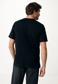 Černé bavlněné tričko s krátkým rukávem, kulatým výstřihem, hladkou texturou a uvolněným střihem, v kombinaci s tmavými džíny.