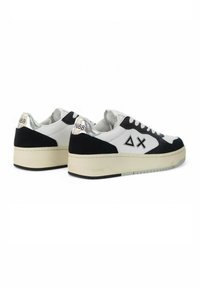 Sneakers bianchi e neri con finitura in suede, dotati di un logo triangolare, dettagli in argento e una suola in gomma spessa con grip testurizzato.