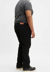 Jeans in denim nero con taglio dritto, con etichetta in pelle sul retro, abbinati a una t-shirt grigia e scarpe nere.