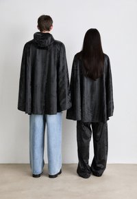 To figurer står med ryggen til, iført sorte satinkapper; den ene i løse blå jeans, den andre i sorte bukser. Teksturen er glatt med en lett glans.