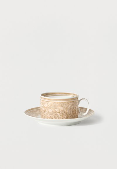 Porcelain teacup with ornate beige and gold floral pattern, paired with matching saucer, set against a plain white background.