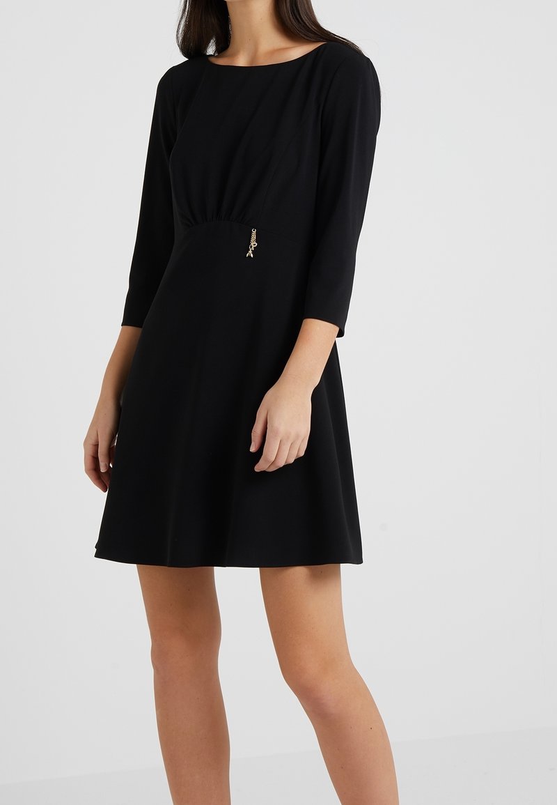 Robe noire à manches trois-quarts, corsage ajusté, jupe évasée et accent doré à la taille. Tissu lisse avec un léger éclat.