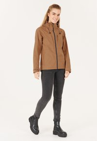 Brun vattentät jacka med dragkedja framtill, justerbar huva och svarta detaljer. Buren med mörkgrå tunna jeans och svarta ankelboots.