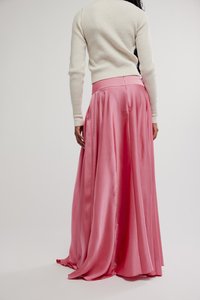 Falda larga de satén rosa con un diseño fluido, que cuenta con bolsillos laterales y una textura suave, combinada con un suéter acanalado de color claro.