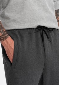 Pantalones de chándal gris oscuro hechos de un tejido suave y texturizado, con bolsillos laterales y una cinturilla ajustable con cordón.