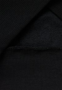 Tejido negro con textura acanalada y un forro interior suave y peludo. Los bordes presentan un dobladillo limpio cosido.