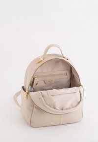 Beżowy plecak ze skóry z złotymi elementami; zapinana główna komora i przednia kieszeń; miękka tekstura i zaokrąglony kształt; w zestawie uchwyt do noszenia.