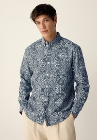 Langärmliges Hemd mit Knöpfen, das ein blau-weißes geometrisches Muster aufweist, aus leichtem Stoff mit klassischem Kragen und lockerer Passform.