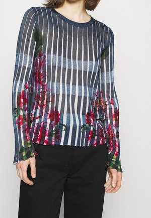 Gennemsigtig bluse med lange ærmer i navy og hvid stribet mønster, med blomstrede detaljer i rødt og grønt, afsluttet med en bølget kant.
