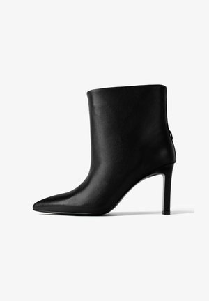 Schwarze Lederknöchelstiefel mit spitzer Zehe und hohem Stiletto-Absatz. Glatte Textur und minimalistisches Design mit einem Reißverschluss auf der Rückseite.