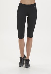 Svarta knälånga atletiska tights med en åtsittande passform, platta sömmar och en bred midjeresår, kombinerade med grå löparskor.