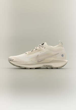 Light beige Nike running shoe with Gore-Tex fabric, trail-specific sole, lace-up design, and pull tab on the heel.