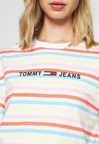 Gestreepte katoenen t-shirt in wit, oranje, groen en geel. Voorzien van geborduurd "TOMMY JEANS" logo op de borst. Ronde hals.